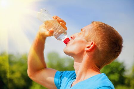 Sport, health and lifestyle concept. Young athletic man after training drinking water from bottle in sun raysの写真素材