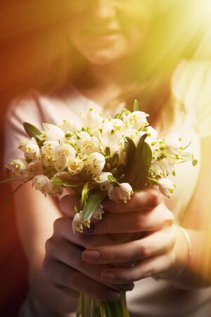 Beautiful young woman with lilies of the valley as symbol of happiness, love and youth.の写真素材