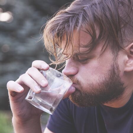 Drinking man. Unhappy sad man sitting outdoors and drinking vodka. の写真素材