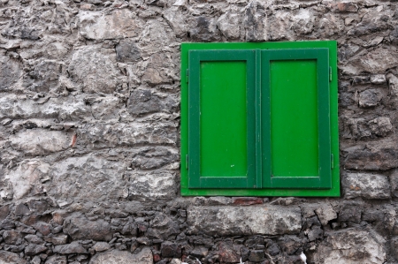 stony house wall with a closed green windowの写真素材