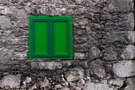 stony house wall with a closed green windowの写真素材