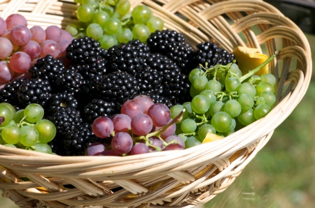 grapes and blackberries in a wooden basket on a glass tableの写真素材