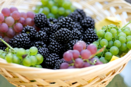 grapes and blackberries in a wooden basket on the glass tableの写真素材
