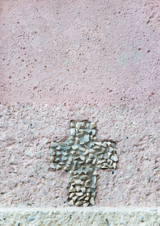 cross made of pebble stones on a rose colored house wallの写真素材