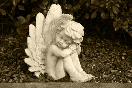 angel made of clay sitting in a hedge on a grave - sepia coloredの写真素材
