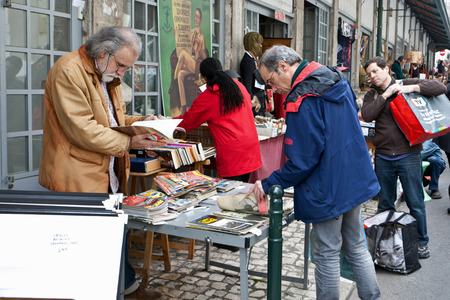 Shoppers wandering through the stalls and displays of consumer goods at an open air market in an urban square in Lisbon city centreのeditorial素材