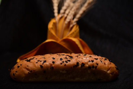 Bread roll and bunch of wheat on black background. food background concept.