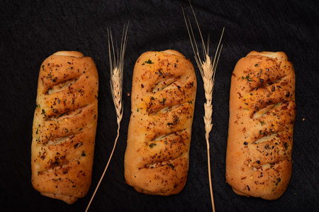 Bread roll and bunch of wheat on black background. food background concept.