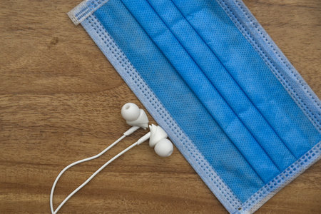 Medical blue face mask and white earphone with wooden background. safety for musician concept.