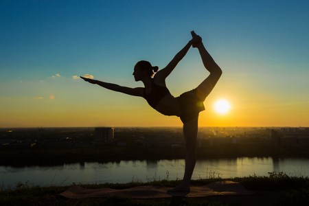 Silhouette of sporty woman practicing yoga in the park at sunset - lord of the dance pose. Sunset light. Freedom, health and yoga conceptの写真素材