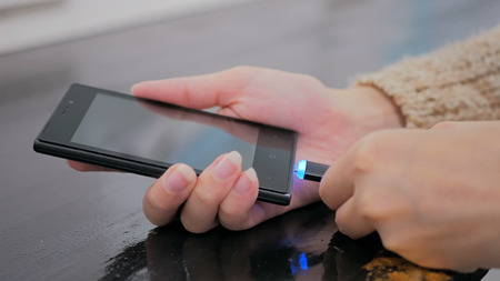 Woman's hand plugging black lightning charging cable into smartphone - USB data cable connecting on modern gadget. Close upの写真素材