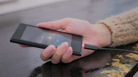 Woman's hand hold smartphone with low battery icon on screen - USB data cable connecting on modern gadget. Close upの写真素材