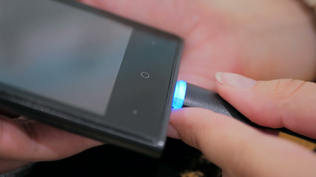 Woman's hand plugging black lightning charging cable into smartphone - USB data cable connecting on modern gadget. Close upの写真素材