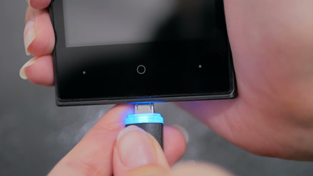 Woman's hand plugging black lightning charging cable into smartphone - USB data cable connecting on modern gadget. Close upの写真素材