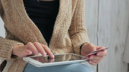 Young woman buying goods from the internet and entering number security code from credit card on digital tablet. Online, technology and internet concept. White wooden backgroundの写真素材