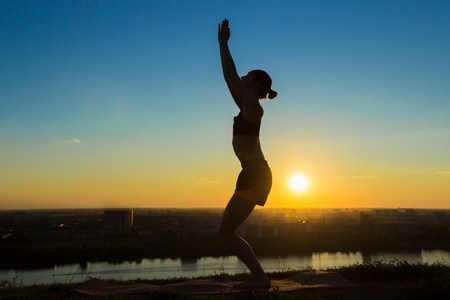Silhouette of sporty woman practicing yoga in the park at sunset. Sunset light, sun lens flares, golden hour. Freedom, health and yoga conceptの写真素材
