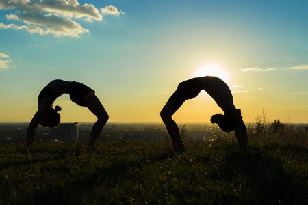 Silhouette of sporty woman and man practicing yoga in the park at sunset - drop back, wheel pose. Sunset light, sun lens flares, golden hour. Freedom, health and yoga conceptの写真素材