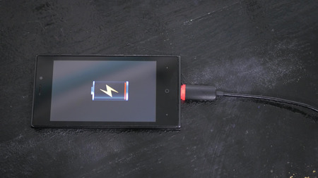 Smartphone with low battery icon on screen - USB data cable connecting on modern gadget. Close upの写真素材