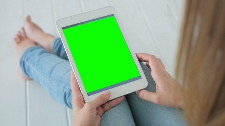 Woman sitting on the white wooden floor and using vertical tablet computer with green screen. Close up shot of woman's hands with pad. Technology and internet conceptの写真素材