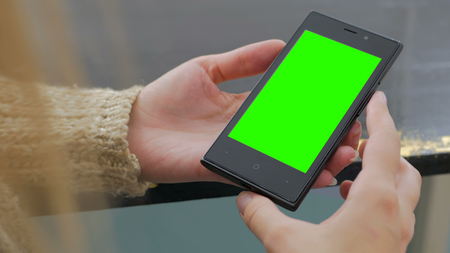 Woman looking at vertical smartphone with green screen. Close up shot of woman's hands with mobileの写真素材