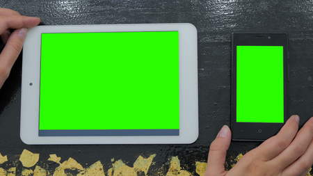 Woman looking at smartphone and digital tablet with green screen. Close up shot of woman's hands with mobile and padの写真素材