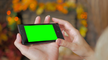 Woman using horizontal smartphone with green screen. Close up shot of woman's hands with mobile. Elegant abstract garlands bokeh backgroundの写真素材
