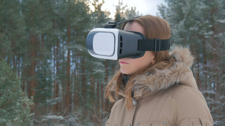 Woman uses a virtual reality glasses in winter forest. Future, nature, winter and technology concept