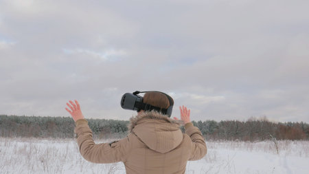 Woman putting on and using virtual reality glasses in winter forest. Virtual reality mask. VR....