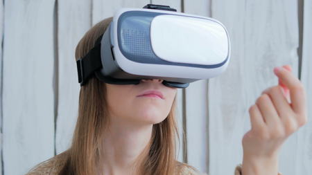 Young woman using Virtual Reality Glasses. Virtual reality mask. VR. White wooden background. Future and technology conceptの写真素材