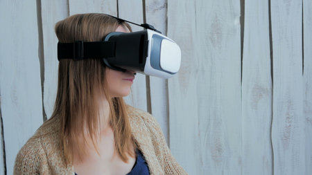 Young woman using Virtual Reality Glasses. Virtual reality mask. VR. White wooden background. Future...