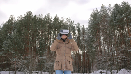 Woman putting on and using virtual reality glasses in winter forest. Virtual reality mask. VR. Future, nature, winter and technology conceptの写真素材
