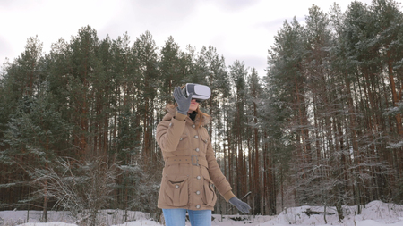 Woman putting on and using virtual reality glasses in winter forest. Virtual reality mask. VR. Future, nature, winter and technology conceptの写真素材