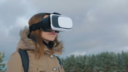 Woman putting on and using virtual reality glasses in winter forest. Virtual reality mask. VR. Future, nature, winter and technology conceptの写真素材
