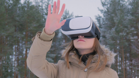 Woman putting on and using virtual reality glasses in winter forest. Virtual reality mask. VR. Future, nature, winter and technology conceptの写真素材