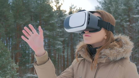 Woman uses a virtual reality glasses in winter forest. Future, nature, winter and technology conceptの写真素材