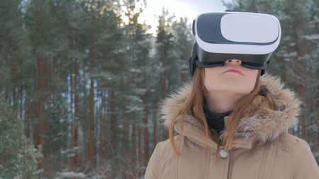 Woman uses a virtual reality glasses in winter forest. Future, nature, winter and technology conceptの写真素材