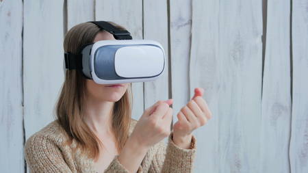 Young woman using Virtual Reality Glasses. Virtual reality mask. VR. White wooden background. Future and technology conceptの写真素材