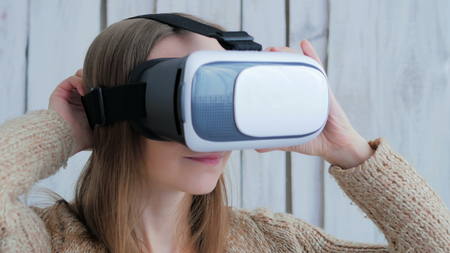 Young woman using Virtual Reality Glasses. Virtual reality mask. VR. White wooden background. Future and technology conceptの写真素材