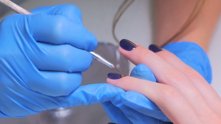 Manicurist treating client at beauty salon. Manicure stage: Painting on the nailの写真素材