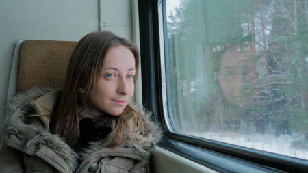 Pensive woman relaxing and looking out of a train window. Travel, transport and winter conceptの写真素材
