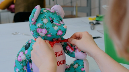 Tailor woman, toymaker tying bow on neck of teddy bear at sewing studio. Handmade, craft and toy making concept. Close up shotの写真素材