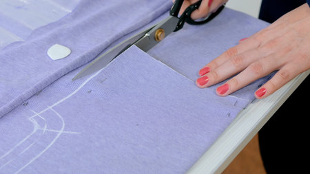 Professional dressmaker, seamstress cutting fabric with scissors at sewing studio. Fashion and...