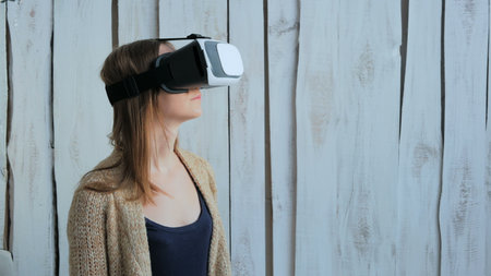 Young woman using Virtual Reality Glasses. Virtual reality mask. VR. White wooden background. Future...