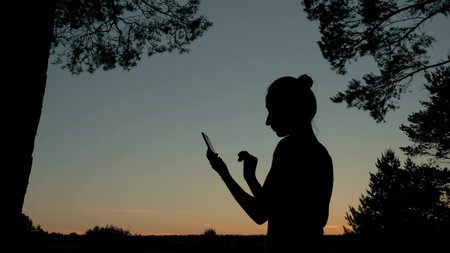 Woman using smartphone in forest after sunset. Relax, nature and technology conceptの写真素材