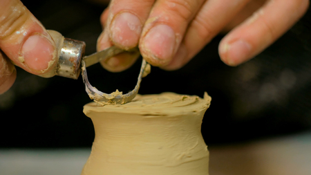 Professional male potter shaping and carving mug with special tool in pottery workshop, studio. Crafting, artwork and handmade conceptの写真素材