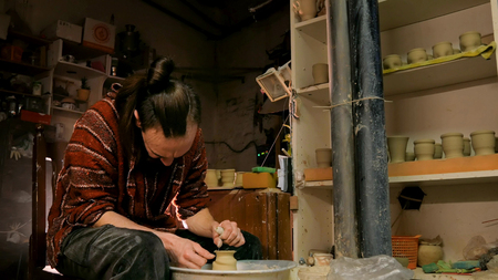 Professional male potter shaping mug with special tool in pottery workshop, studio. Crafting, artwork and handmade conceptの写真素材