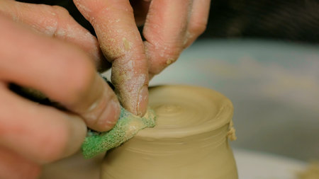 Professional male potter shaping mug with special tool in pottery workshop, studio. Crafting,...
