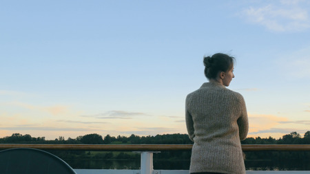 Woman standing on deck of cruise ship and looking at landscape after sunset. Relax, nature and journey conceptの写真素材