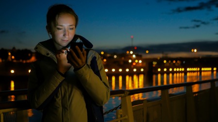 Woman using vertical smart phone on deck of cruise ship at night. Relax, technology and journey conceptの写真素材