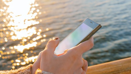 Woman using smartphone on deck of cruise ship at sunset. Sunset light, golden hour. Technology and journey conceptの写真素材